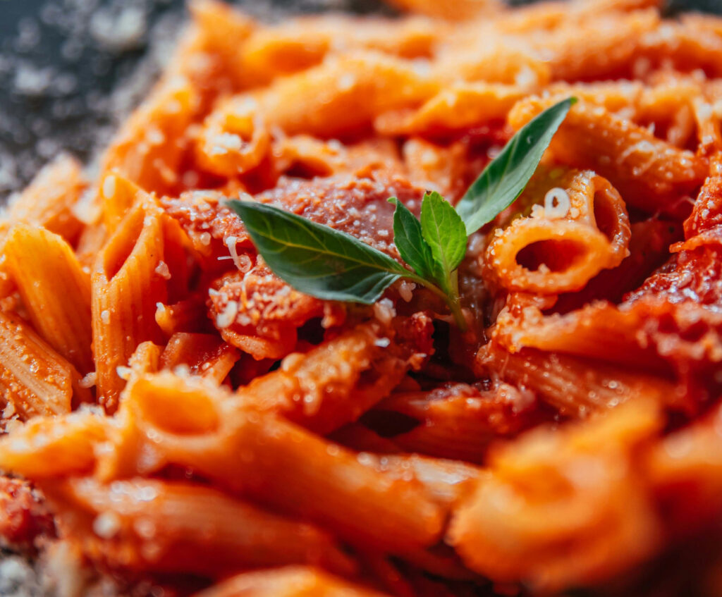 Close up of penne pasta with tomato sauce and basil garnish