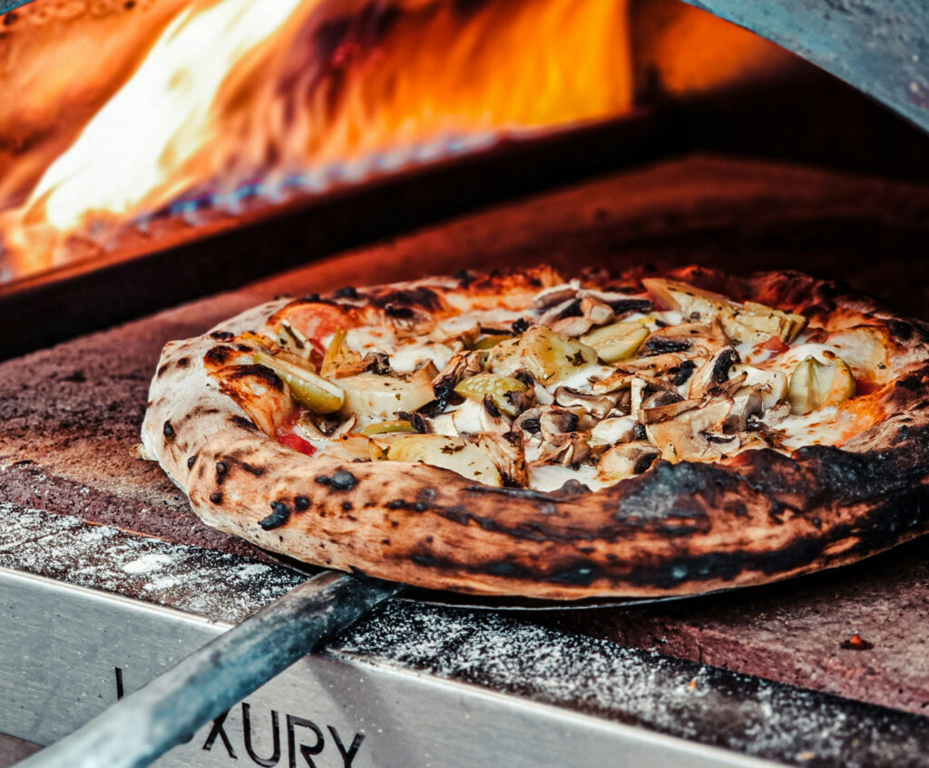 Close up of pizza in oven on pizza board with flames in the background