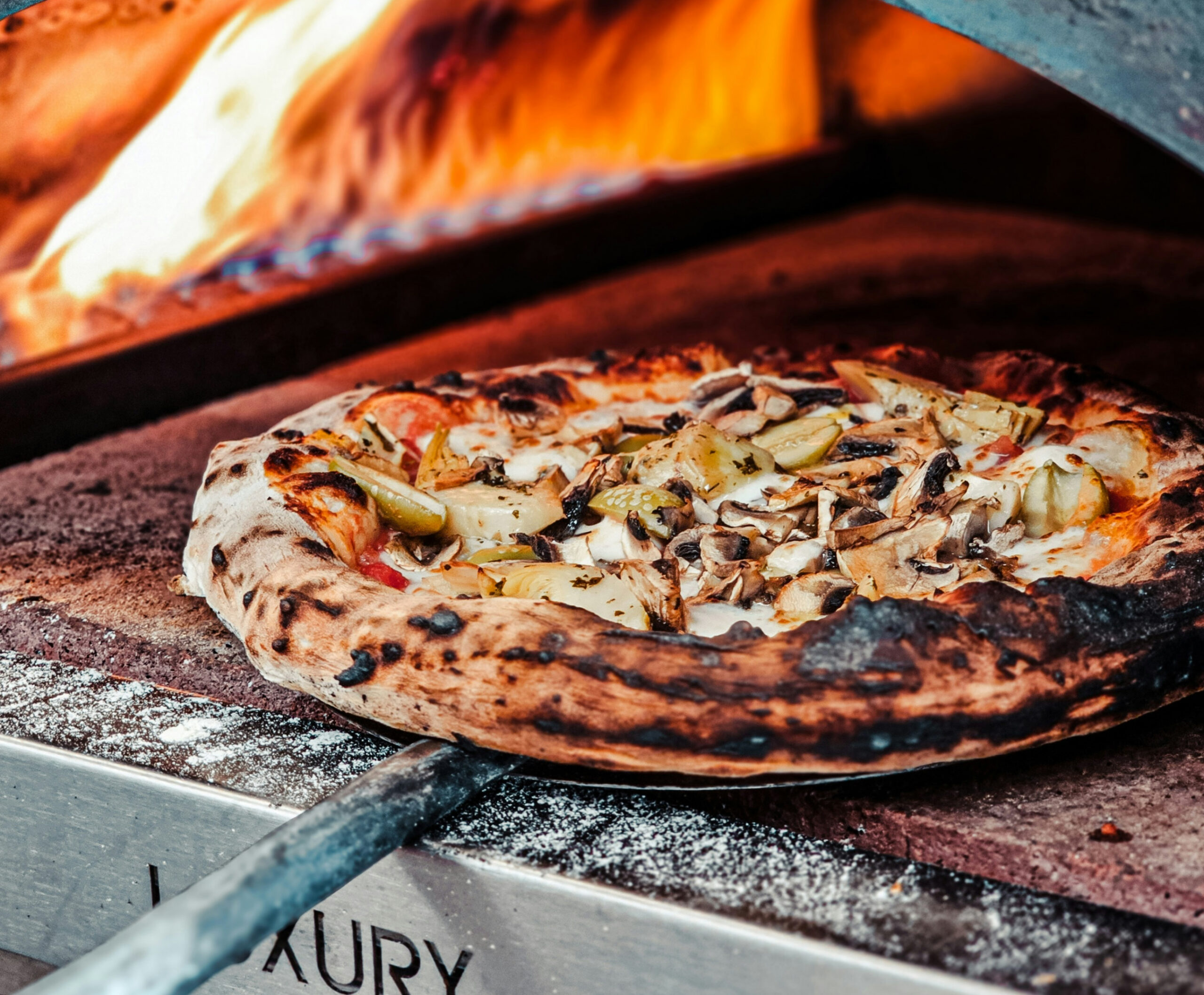 Close up of pizza in oven on pizza board with flames in the background