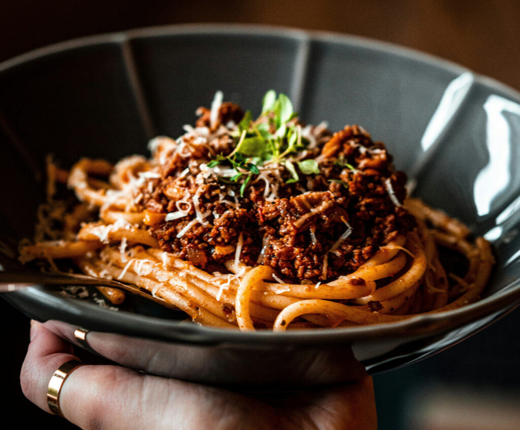 Close up of noodles with chopped meat and greens in ceramic bowl