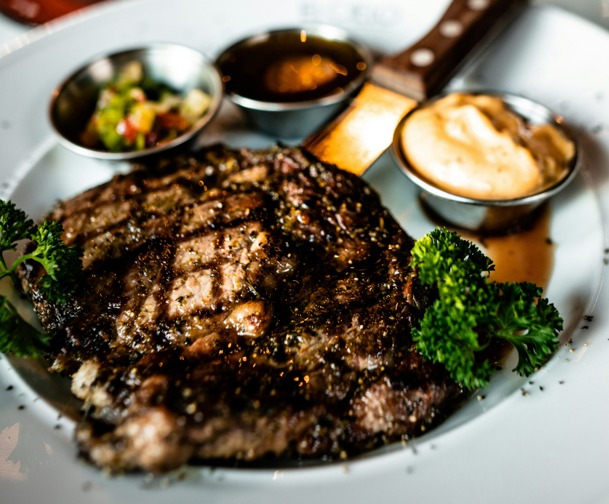 Close up of grilled meat with dipping sauces on white plate with steak knife