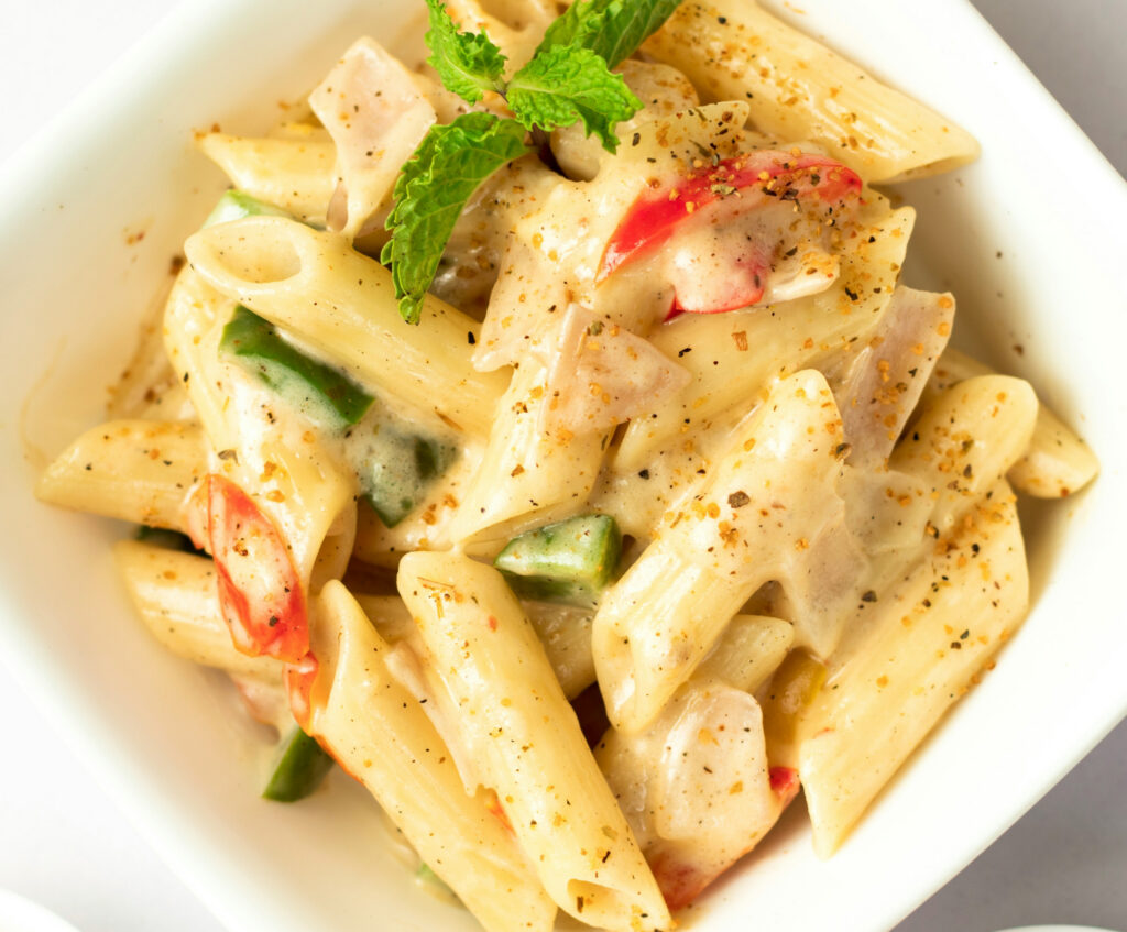 Close up of penne pasta in white sauce with greens and tomatoes