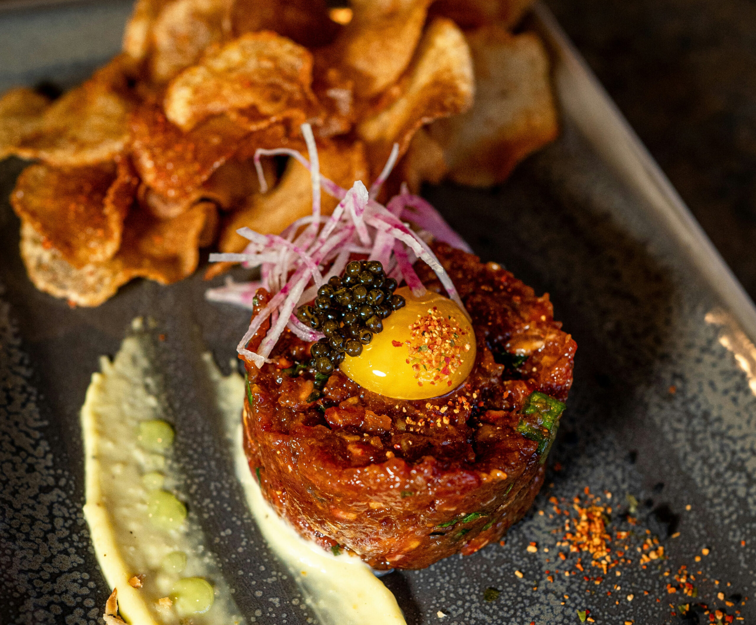 Close up of artful meal with egg, sliced onion, caviar, and potato chips on ceramic plate