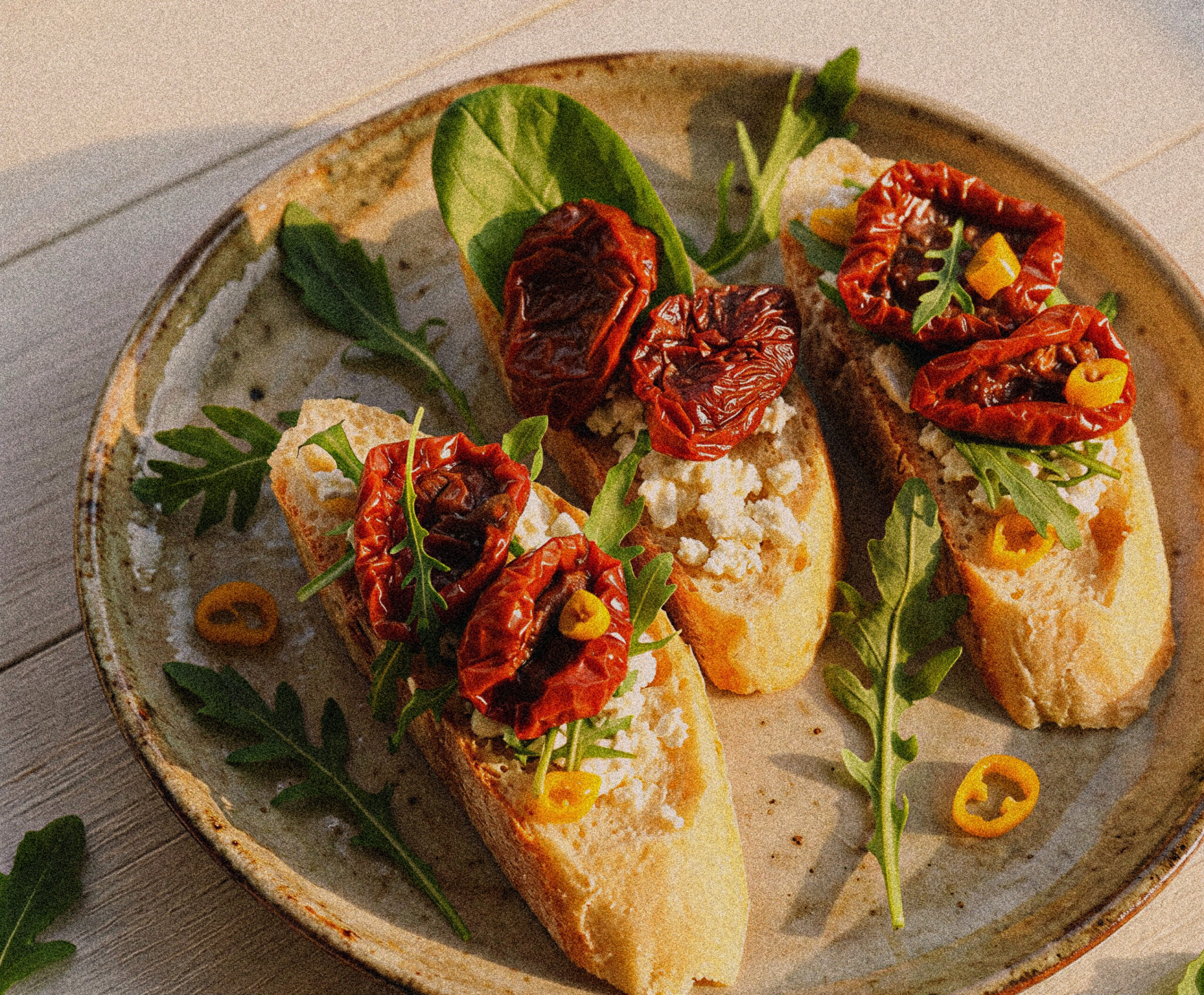 Close up of bruschetta with dried tomatoes, cheese, and arugula on a ceramic plate