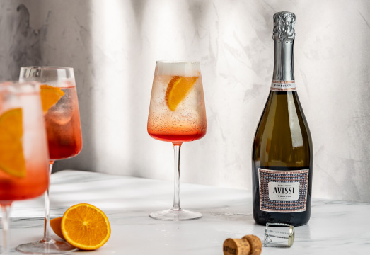 Table top arrangement of cocktail glasses full of spritz cocktail and a bottle of Avissi Prosecco