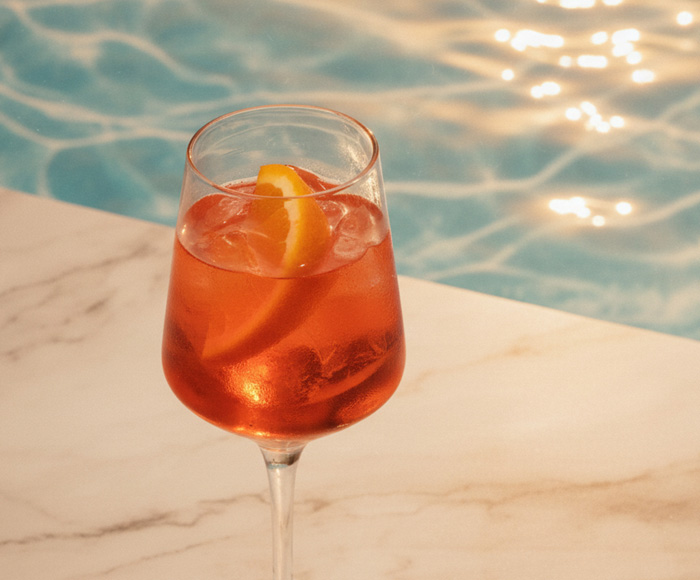 Close up of an aperol spritz cocktail in stemware on a marble surface with sparkling water in the background