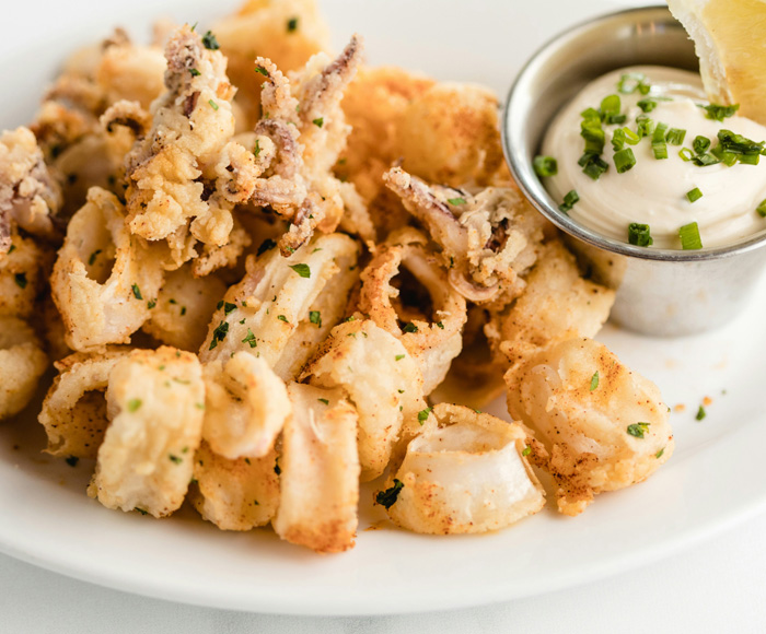 Close up of fried calamari and dipping sauce on white plate