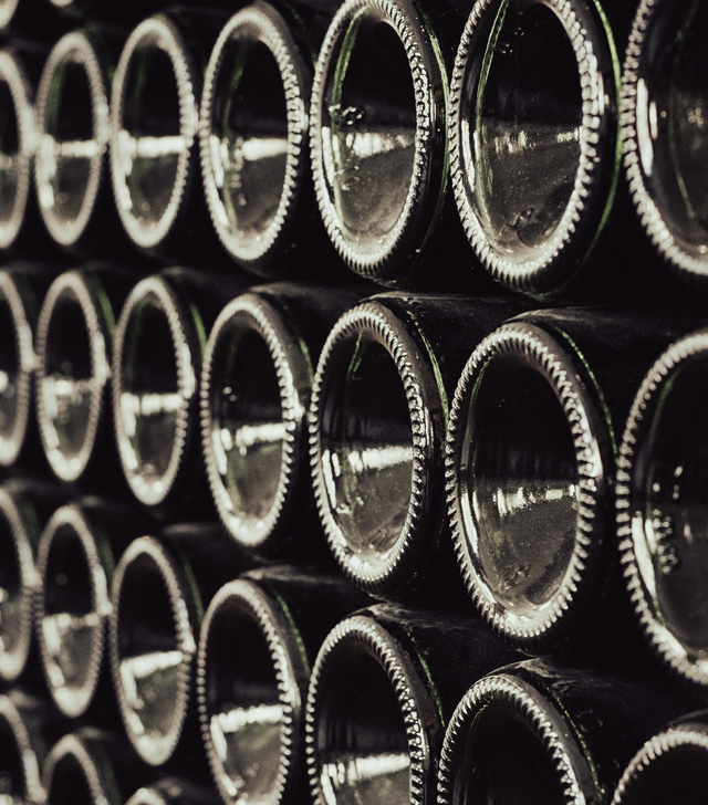Close up of the bottom ends of Prosecco bottles that are stacked horizontally in a grid pattern